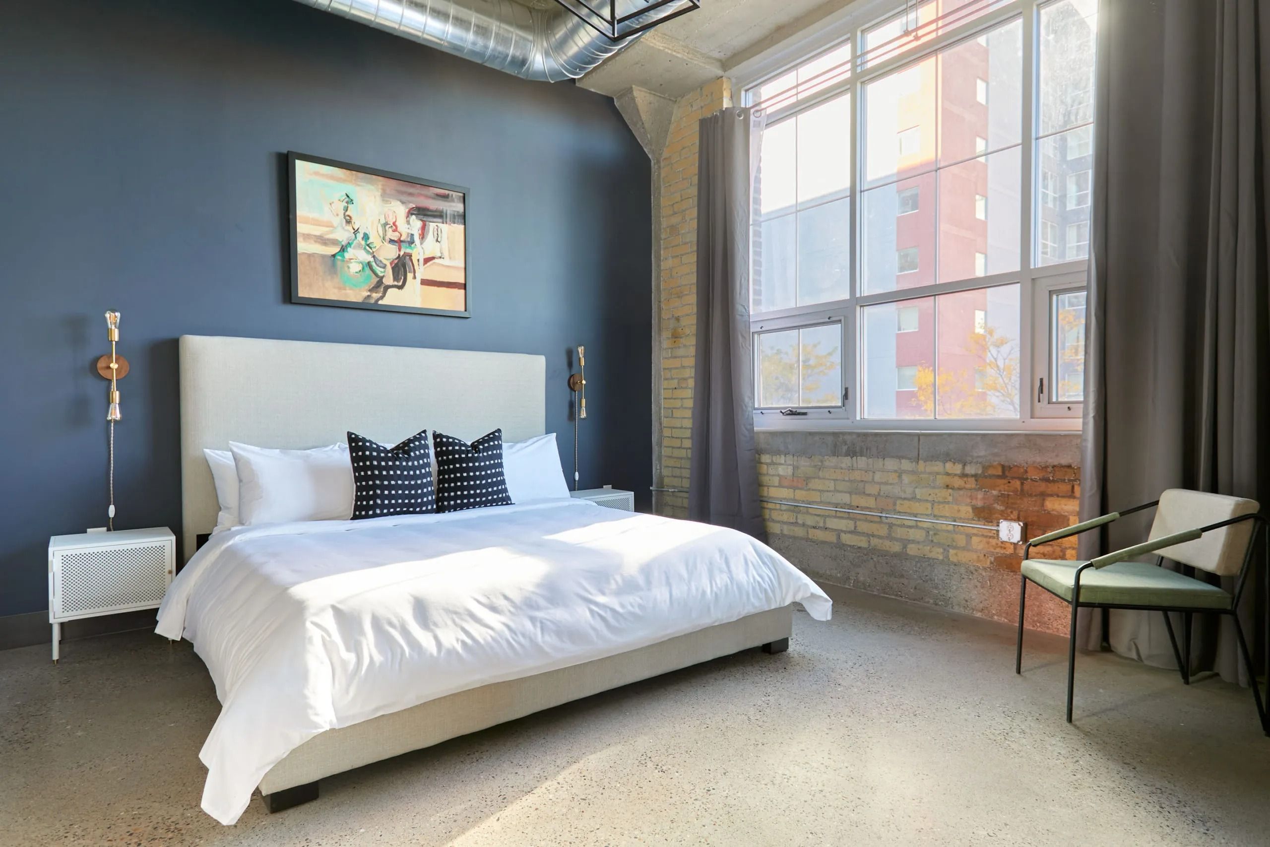 Large bed inside MAX apartments bedroom with large windows and a blue accent wall